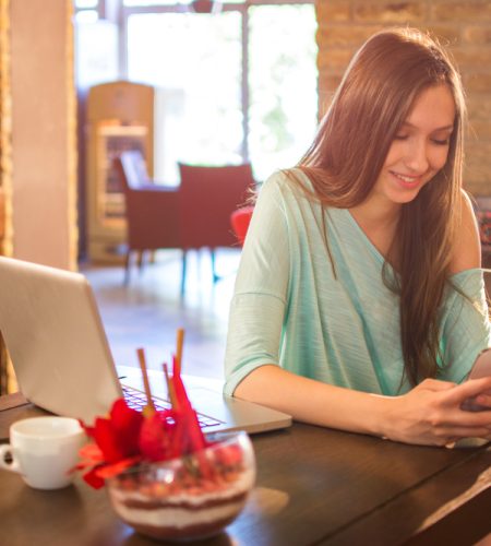 About young,woman,using,mobile,phone,and,laptop,in,a,cafe